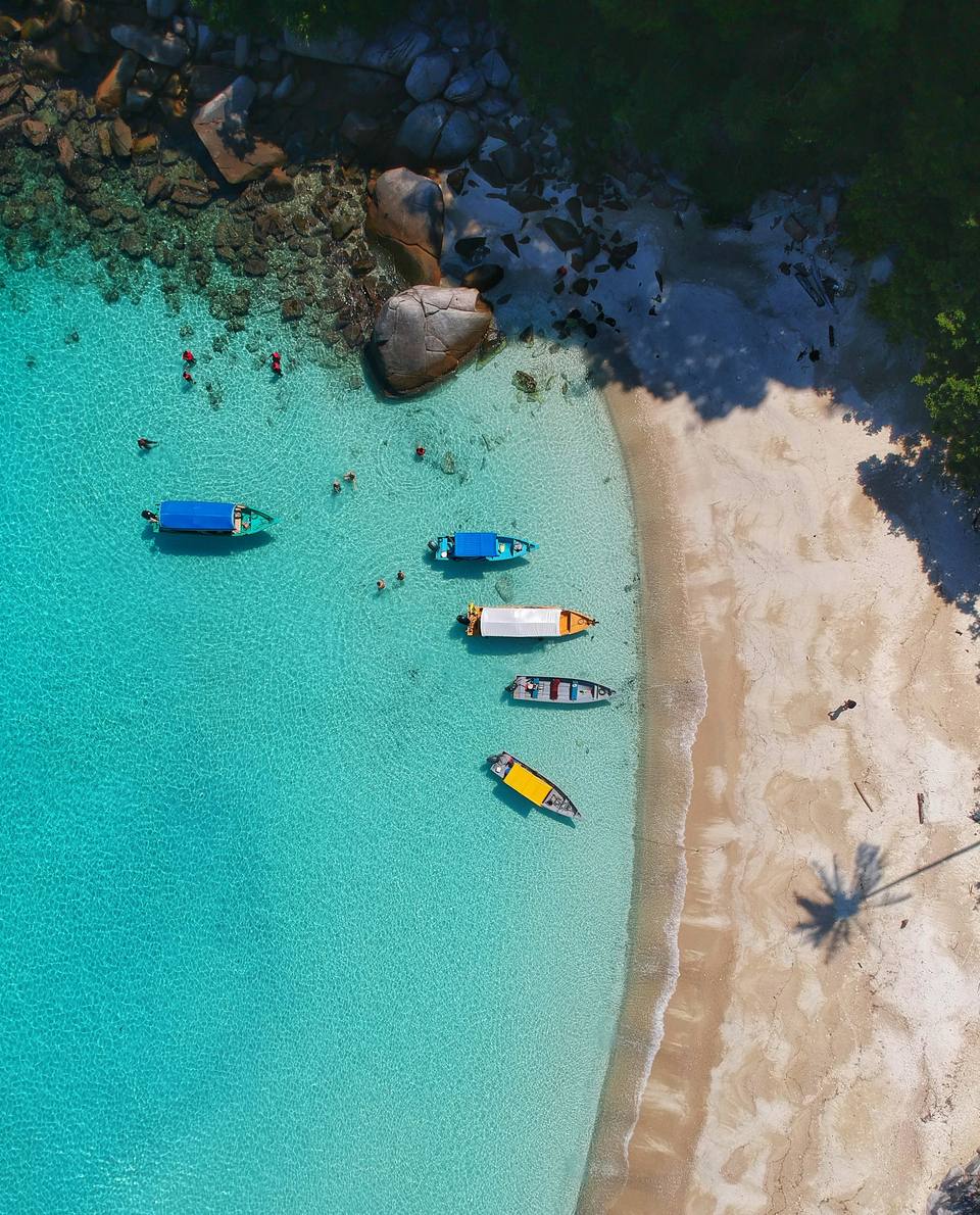 Turquoise cove with boats moored off a sandy beach, from above